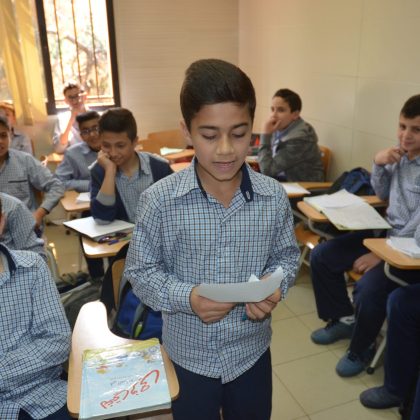 A class full of students. One of the student is standing and reading out of paper.